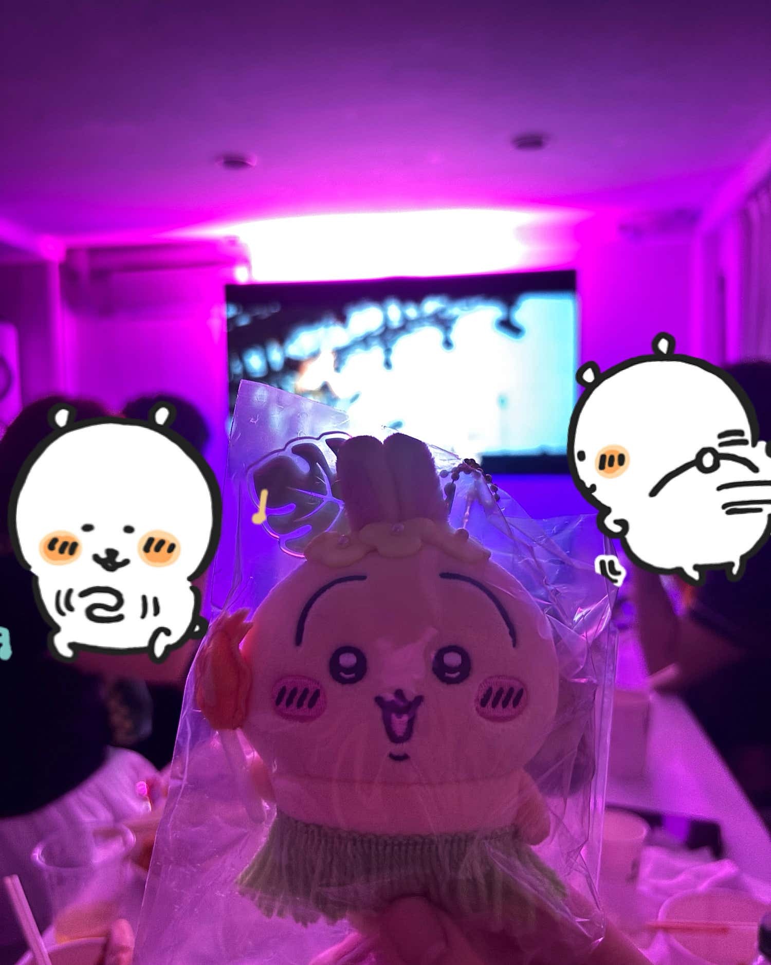 캐릭터 소품 뒤로 영상 화면과 보라색 실내 조명이 보이는 모습
