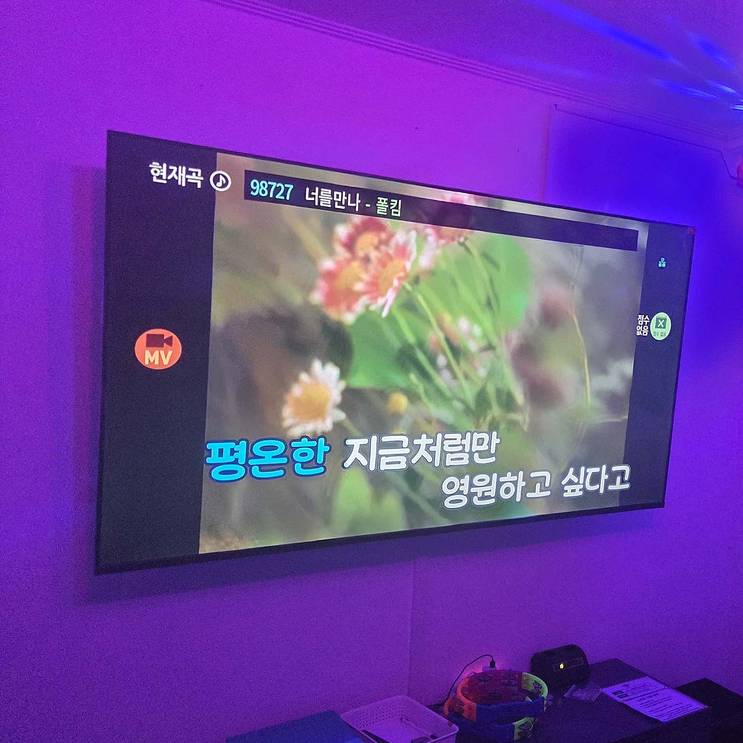 보라색 조명 아래 노래 화면과 벽면 TV가 보이는 모습