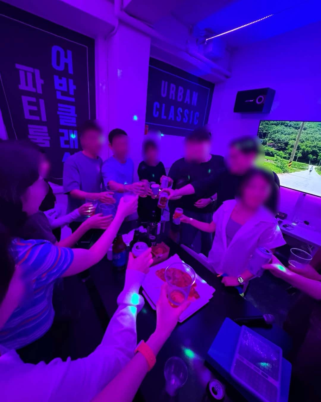 보라색 조명 아래 여러 사람이 잔을 들고 모인 노래 공간
