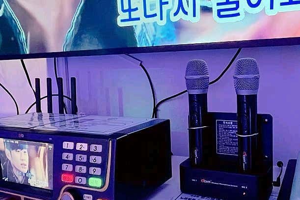 노래 기기 조작부와 충전 거치대에 꽂힌 무선 마이크 두 개