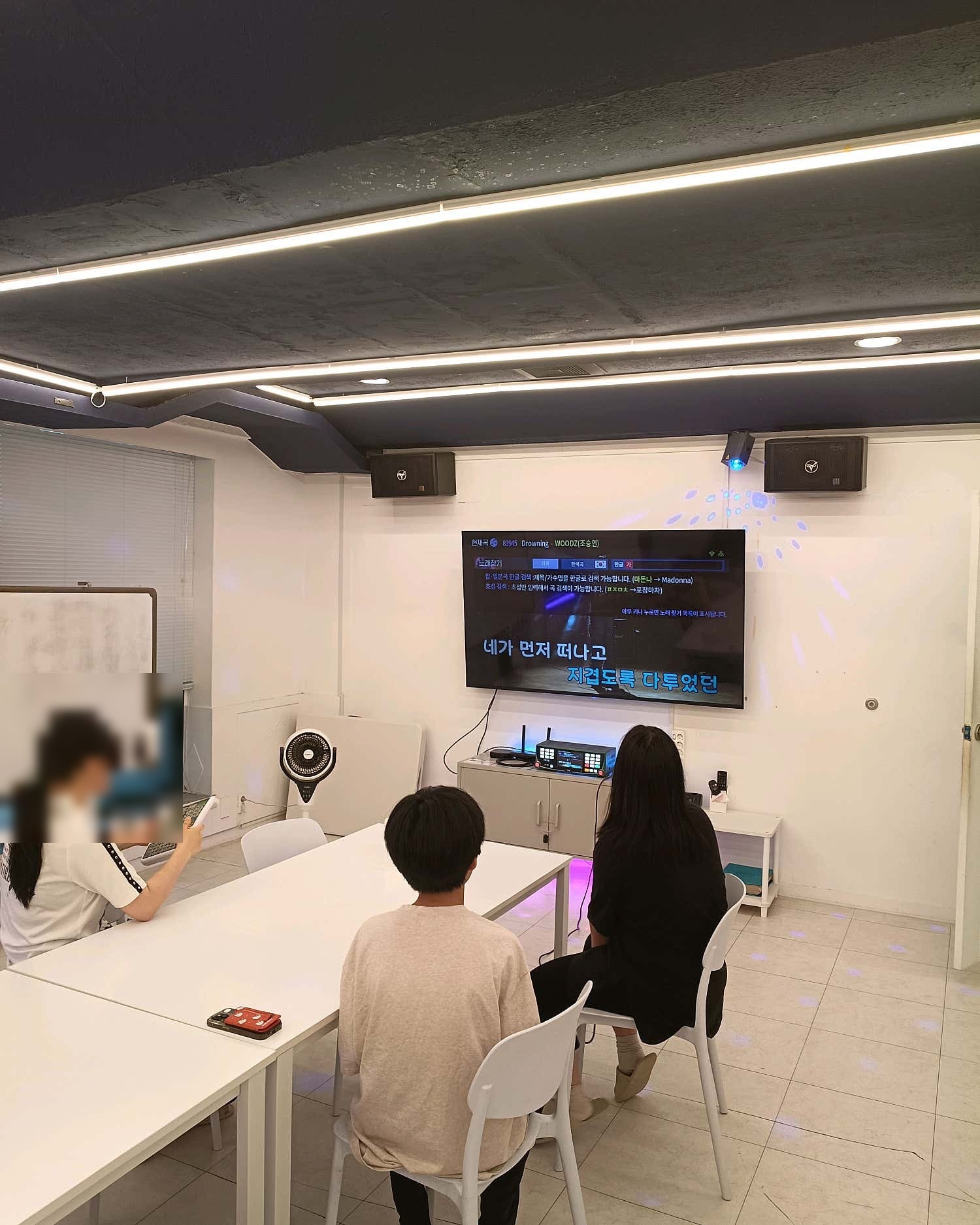 긴 흰색 테이블에 앉아 화면을 바라보는 이용자 세 명