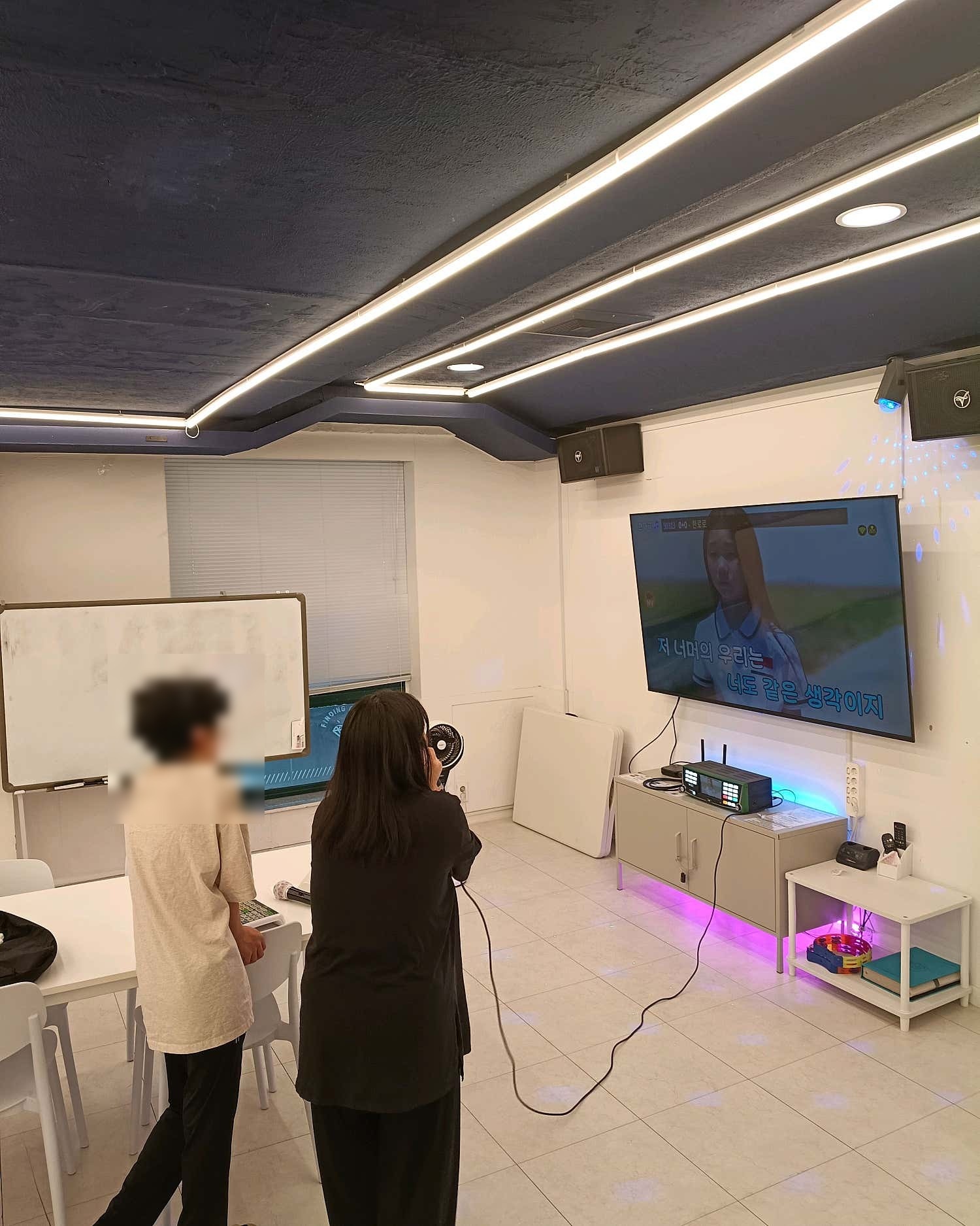 이용자 한 명과 뒷모습 이용자 한 명이 화면 앞에서 노래하는 모습