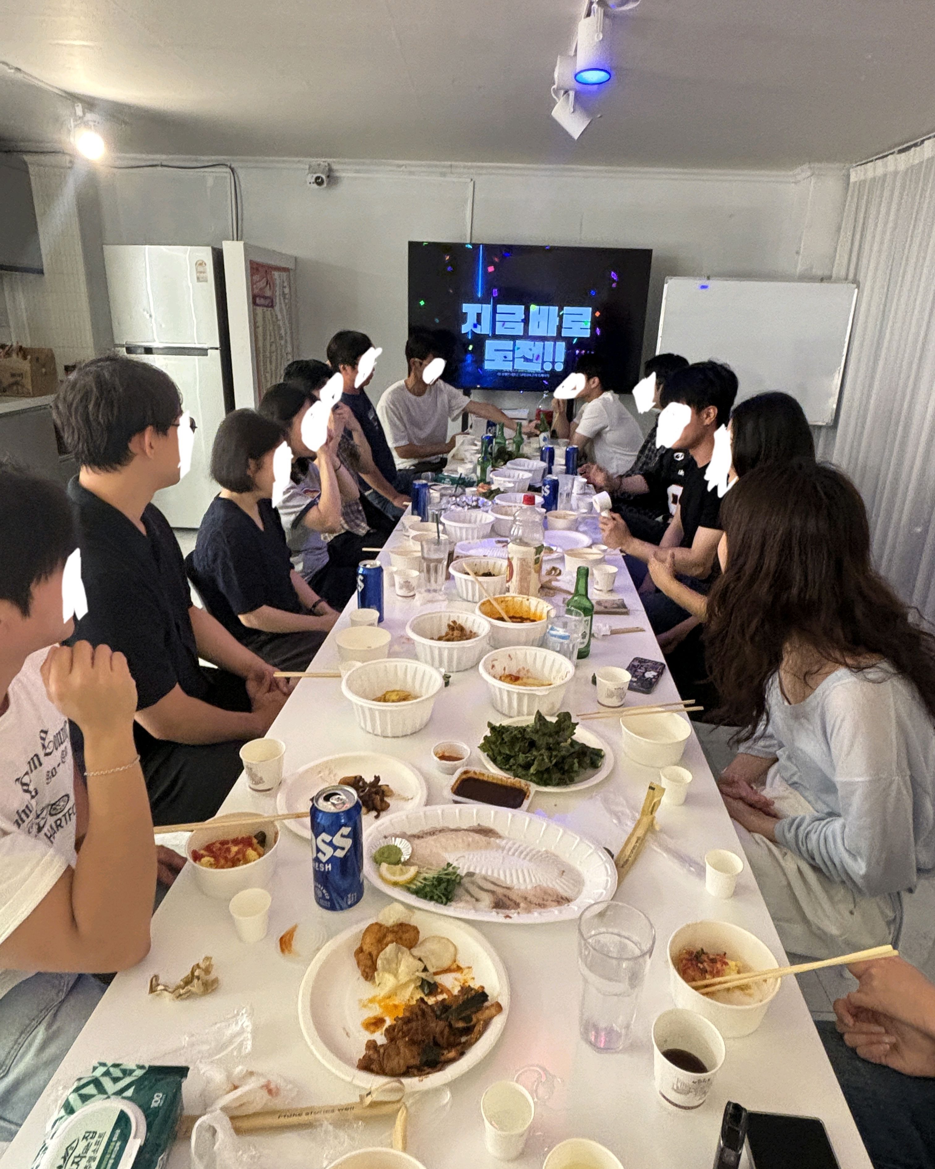 음식이 놓인 긴 테이블과 화면을 함께 바라보는 단체