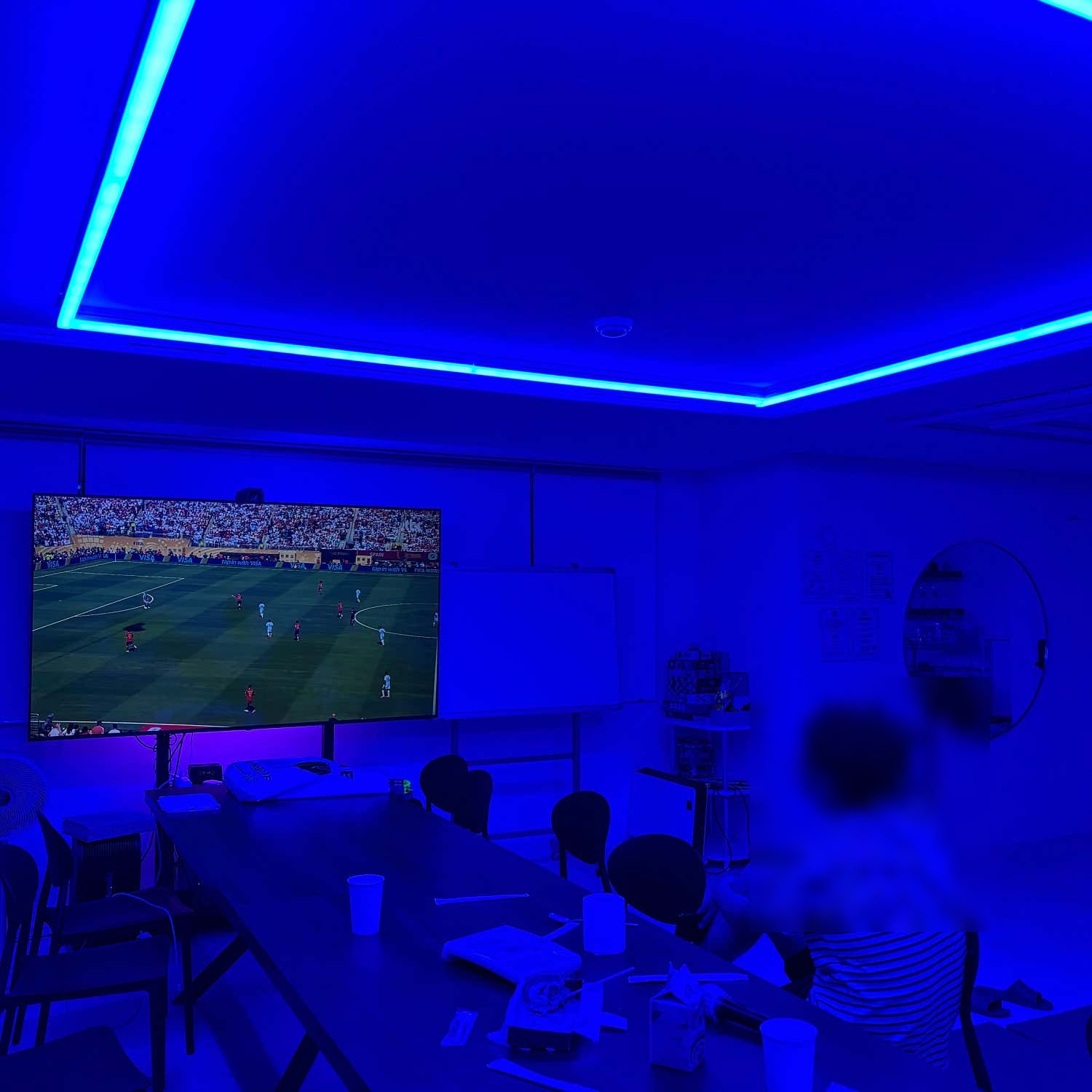푸른 조명 아래 큰 화면으로 축구 경기를 함께 보는 자리